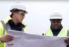 Male apprentice looking at blueprints on site with his employer