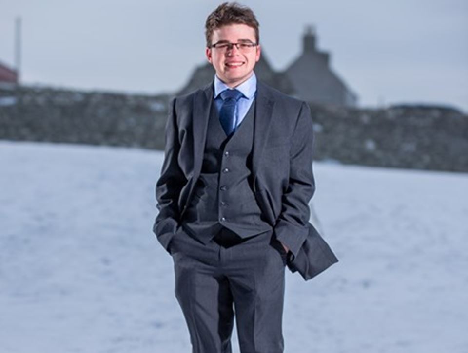 Young person wearing suit, tie and glasses standing in front of a snowy backdrop